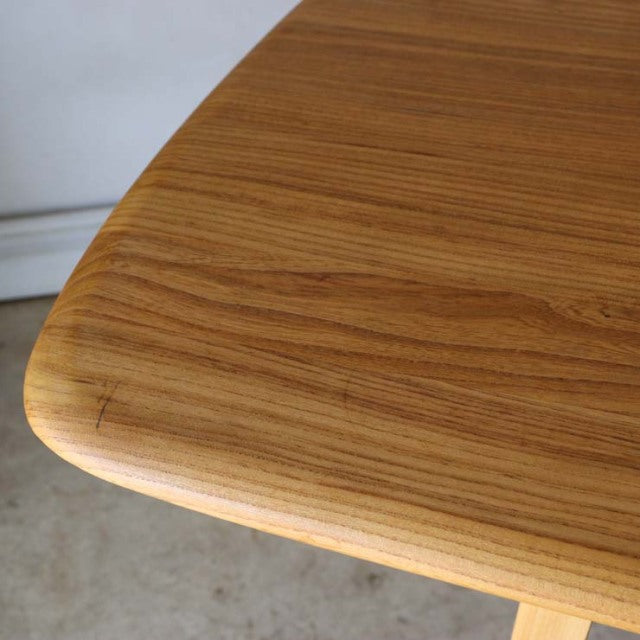 Mid-century British Ercol dining table corner in warm teak with smooth rounded edge and visible wood grain.
