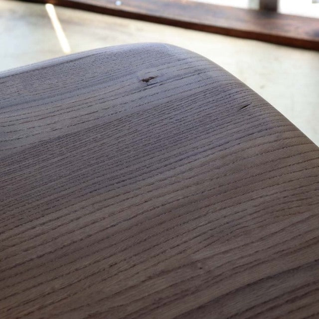 Close-up of vintage British mid-century teak dining table top showing smooth wood grain and rounded corner.