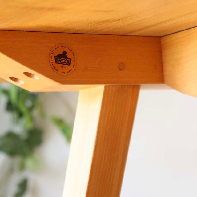Close-up of vintage British mid-century teak dining table leg showing natural wood grain and Ercol brand stamp on smooth,.