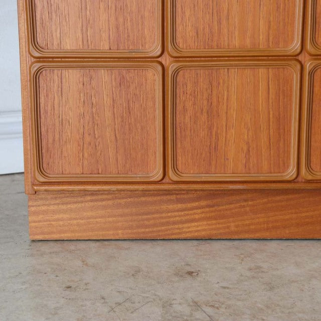 Close-up of vintage British teak sideboard front showing mid-century carved square panel details and rich wood grain with.