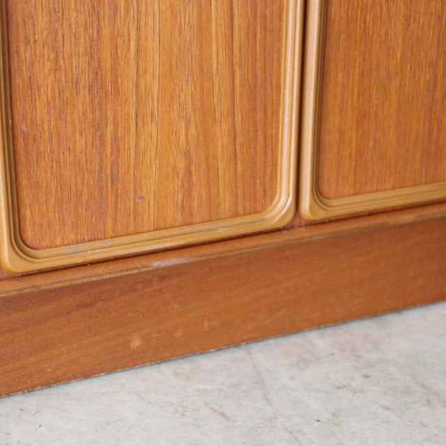 Close-up of vintage British McIntosh teak sideboard door with smooth wood grain and mid-century rounded edges on a sturdy.