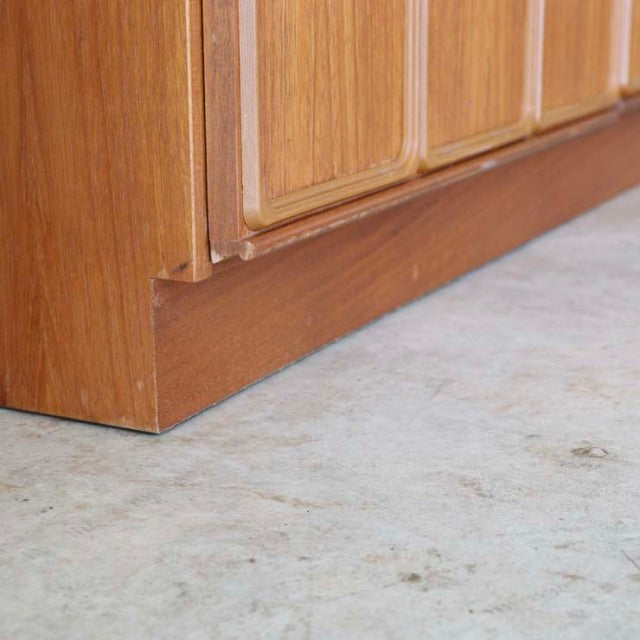 Close-up of vintage British McIntosh teak sideboard base showing rich wood grain and smooth mid-century craftsmanship.