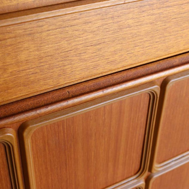 Close-up of vintage British McIntosh teak sideboard showing rich wood grain and mid-century sculpted panel detail.