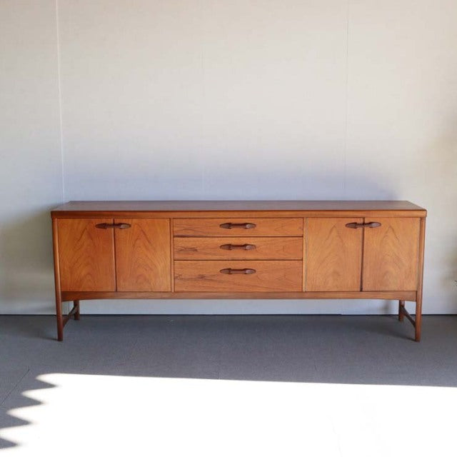 Vintage mid-century teak sideboard by British brand Nathan with clean lines, three central drawers, two doors, and tapered.