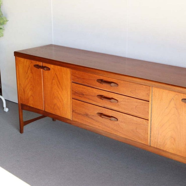 Vintage teak Nathan mid-century sideboard with rich wood grain, three central drawers, and two cupboard doors, slender legs, .