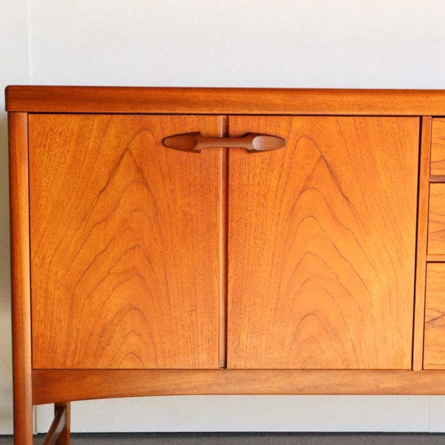 Mid-century teak sideboard by British brand Nathan with smooth wood grain, rounded edges, and tapered legs.