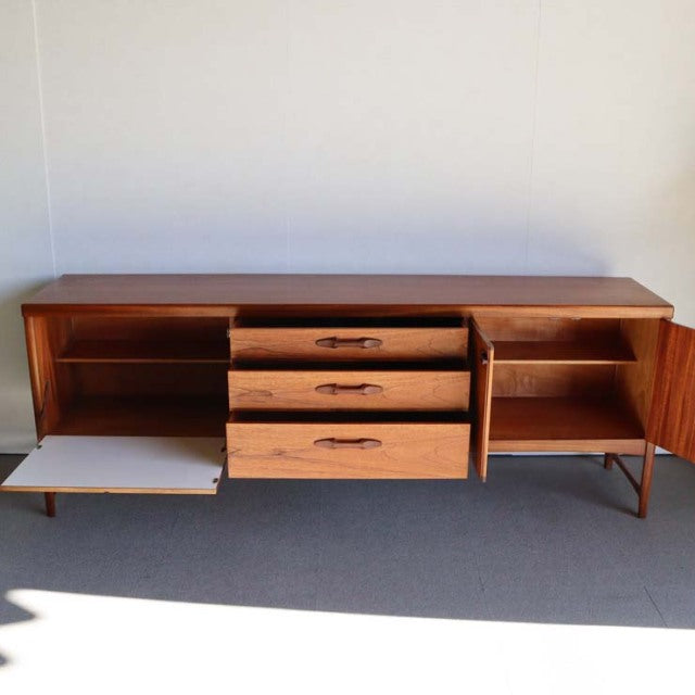 Mid-century British teak sideboard by Nathan with three center drawers, open compartments, and visible wood grain.