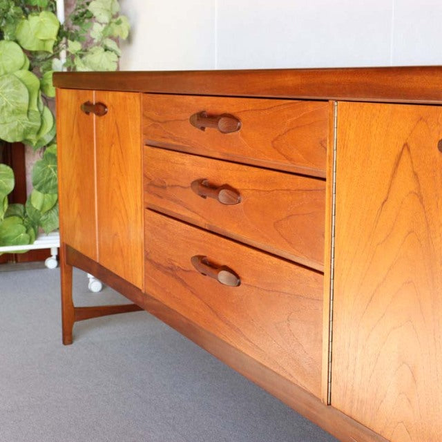 Mid-century vintage teak sideboard by British Nathan with smooth wood grain, three central drawers, rounded wooden handles,.