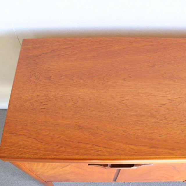Vintage Nathan teak sideboard with smooth grain, mid-century British and Danish style, clean lines, sleek wooden legs.