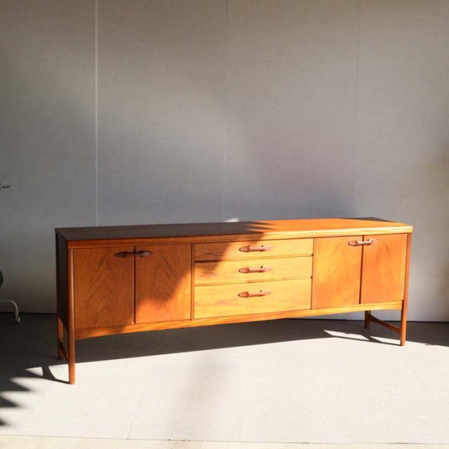 Mid-century British teak sideboard by Nathan with rich wood grain, three central drawers, and flared legs, showcasing.