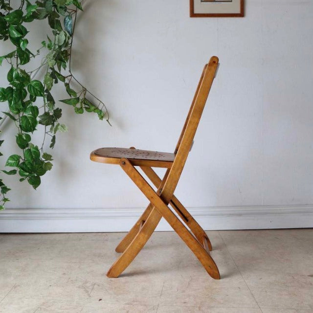 Mid-century British teak folding chair with warm wood grain and simple X-frame legs against white wall.