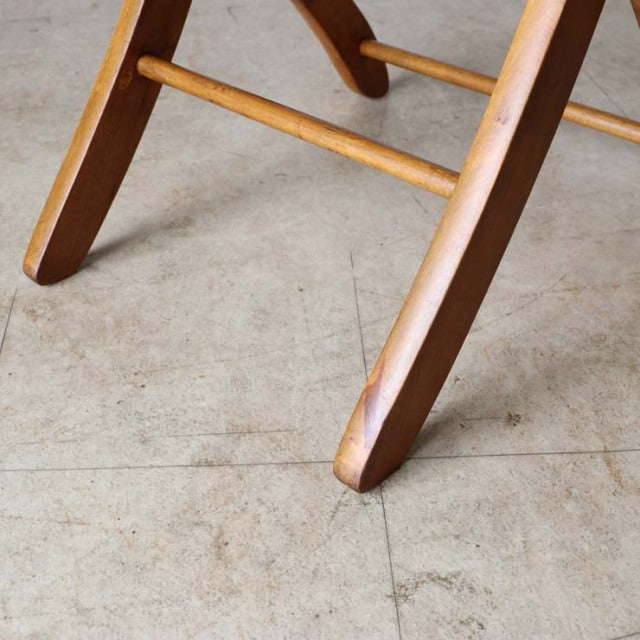 Close-up of vintage teak British mid-century folding chair legs with smooth wood grain and rounded edges on concrete floor.