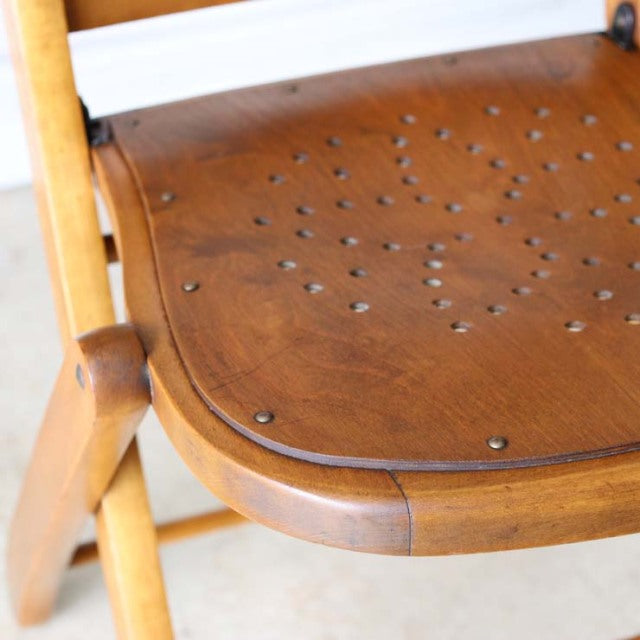 Vintage teak folding chair with perforated seat, mid-century British design, smooth wood grain and sturdy angled legs.