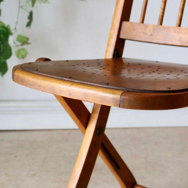 Mid-century vintage British teak folding chair with curved seat, perforated wood grain, and crossed legs.