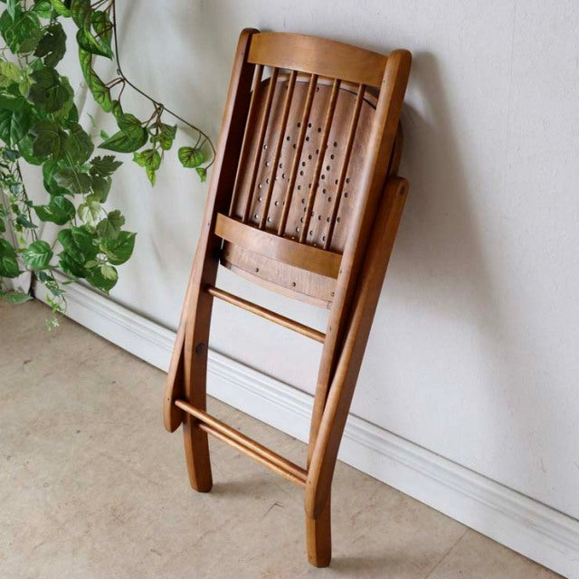 Mid-century British vintage teak folding chair with vertical slats and smooth finish, leaning against wall.