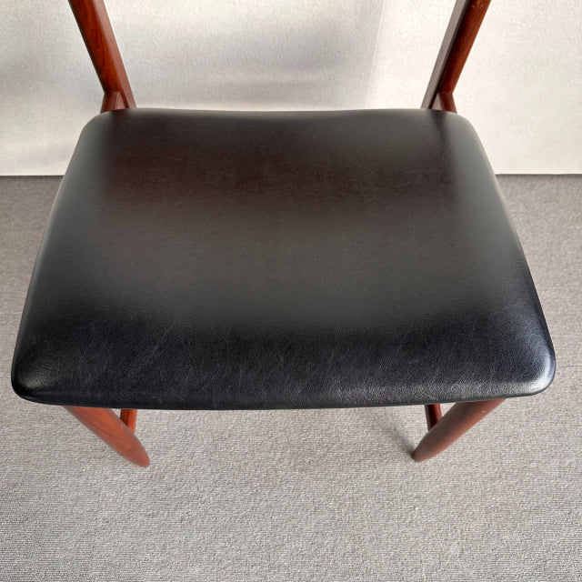 British mid-century dining chair with smooth black leather seat and warm teak wood frame showing rich grain.