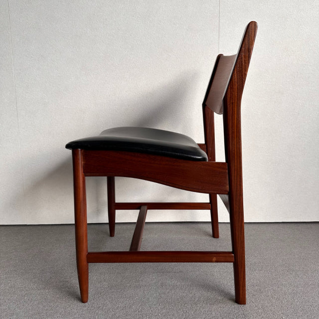 Mid-century British vintage dining chair in rich teak wood with sleek black leather seat and minimalist tapered legs.