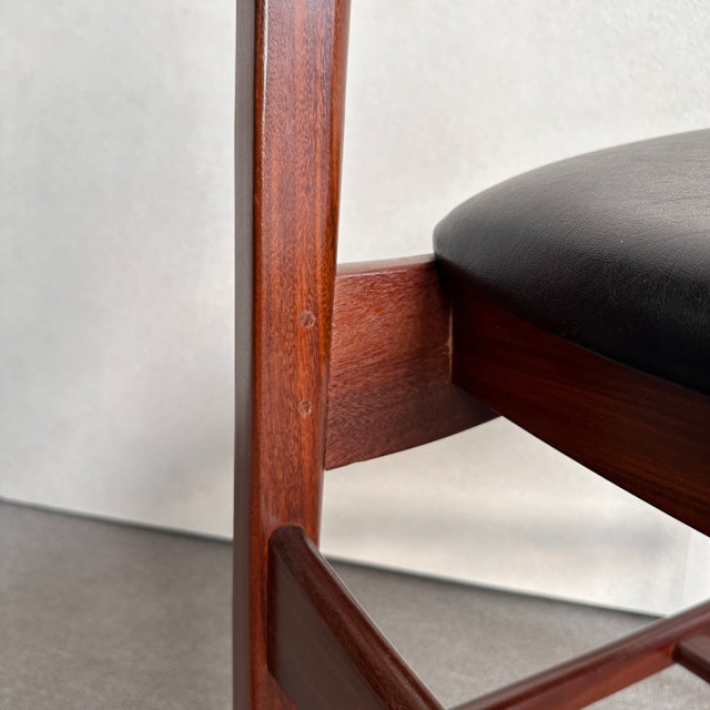 Mid-century British vintage teak dining chair leg with rich wood grain and black leather seat edge.
