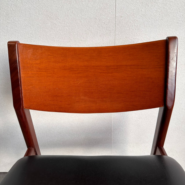 Vintage British mid-century dining chair with teak wood backrest and black leather seat, sleek angled legs.