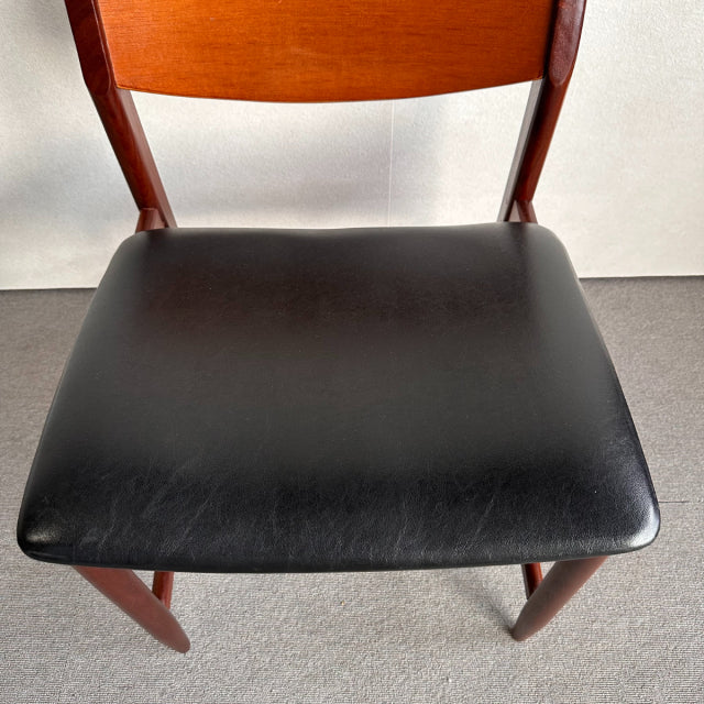 Mid-century British vintage dining chair with teak frame and black leather seat, smooth wood grain and tapered legs.