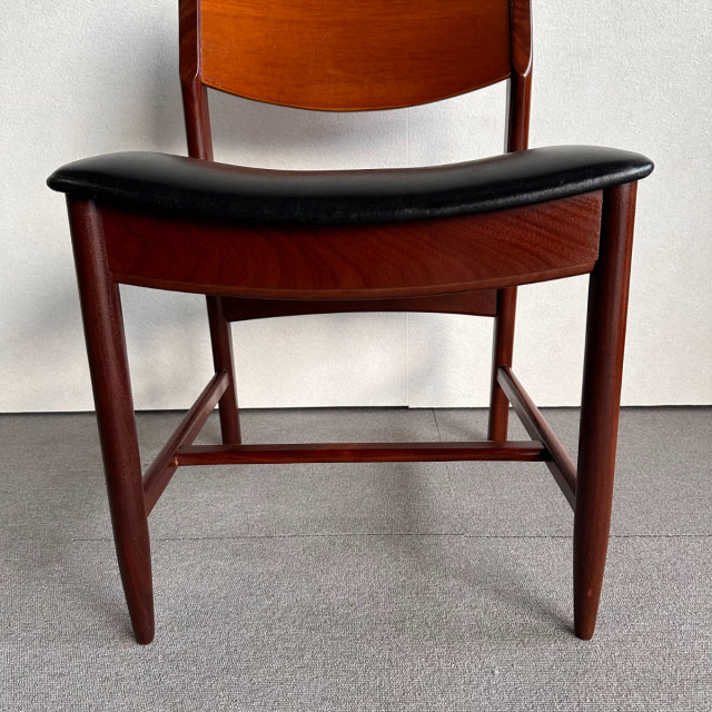 Mid-century British vintage dining chair in teak with black leather seat, sleek wood grain and tapered legs.