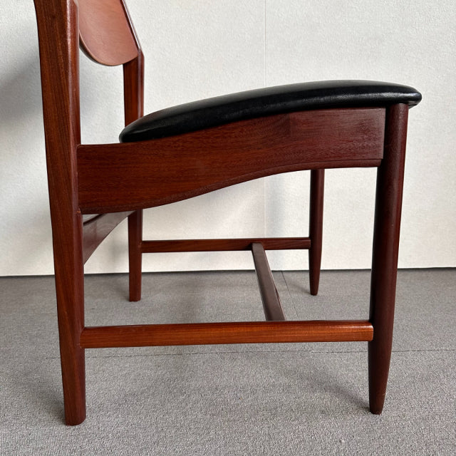 Mid-century British vintage dining chair with rich teak wood frame and smooth black leather seat cushion, showcasing clean.