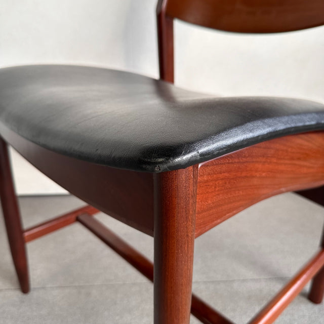 Vintage British mid-century dining chair with teak frame and black leather curved seat, smooth wood grain and tapered legs,.