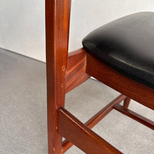 Close-up of vintage British teak dining chair leg with visible wood grain and black leather seat cushion showing mid-century .