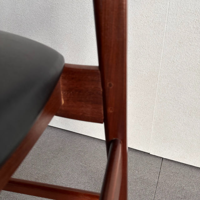 Mid-century British vintage dining chair with rich teak wood frame and smooth black leather seat, showcasing warm wood grain .