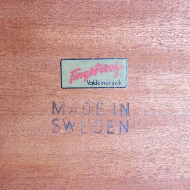 Close-up of teak wood grain with Fleming & Valdemarsvik label and "Made in Sweden" stamp, highlighting vintage mid-century.