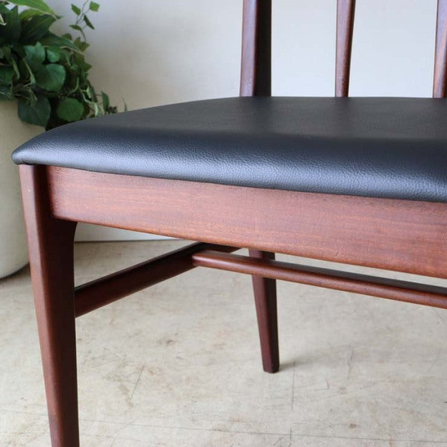 Vintage teak dining chair with black leather cushion, British mid-century style, slender tapered legs, and visible wood grain.