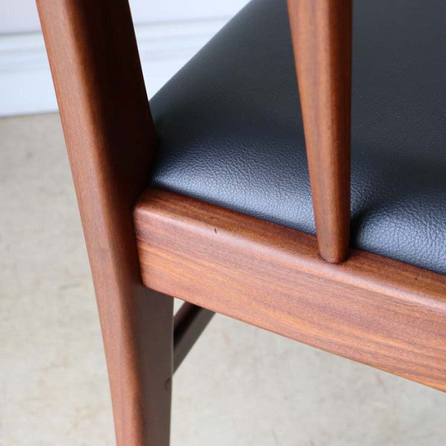 Mid-century vintage teak dining chair with British design, smooth wood grain, and black leather seat upholstery.
