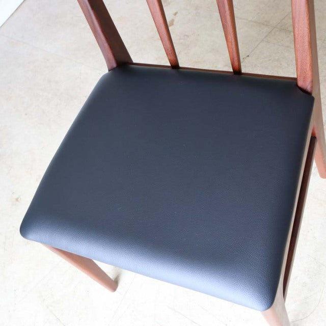 Set of four British mid-century teak dining chairs by John Herbert Fonseca, black cushioned seats, slender vertical back.