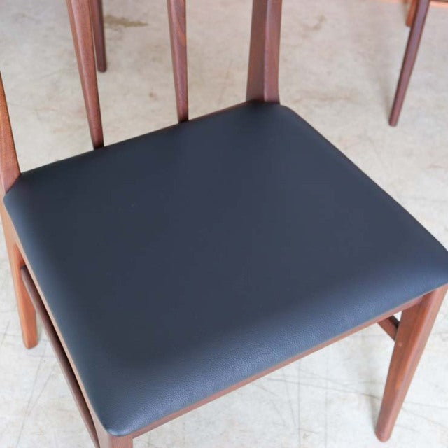 Mid-century British teak dining chair with smooth black leather seat and tapered wood legs.