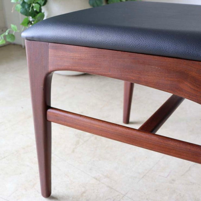 Vintage teak dining chair leg and frame with smooth grain, mid-century British Denmark style, black cushioned seat.