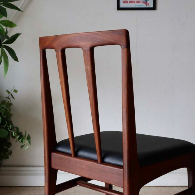 Set of four British mid-century dining chairs in vintage teak with black leather seats and sleek tapered legs.