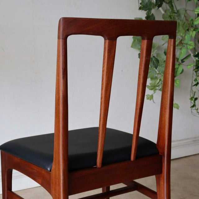 Vintage teak dining chair with British mid-century design, slender vertical back slats, black cushioned seat, and tapered.