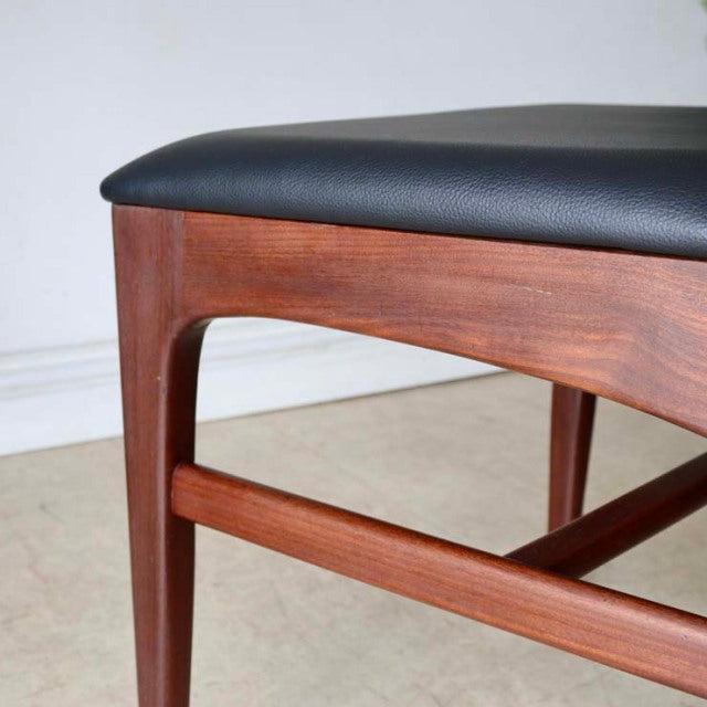 Vintage teak dining chair corner showing smooth wood grain and rich mid-century British design with black upholstered seat.