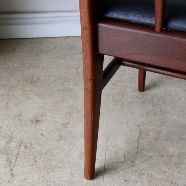Mid-century British dining chair leg in teak with smooth grain and dark upholstered seat corner.