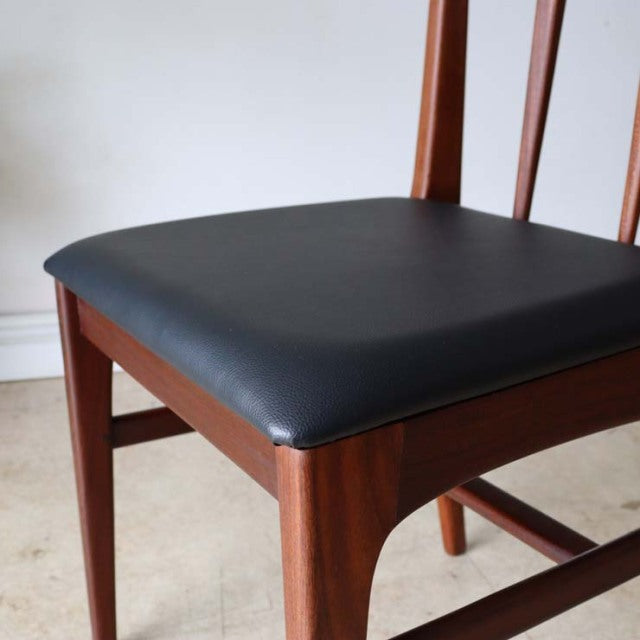 Vintage teak dining chair with black cushioned seat, slender legs, and mid-century British-Denmark design.