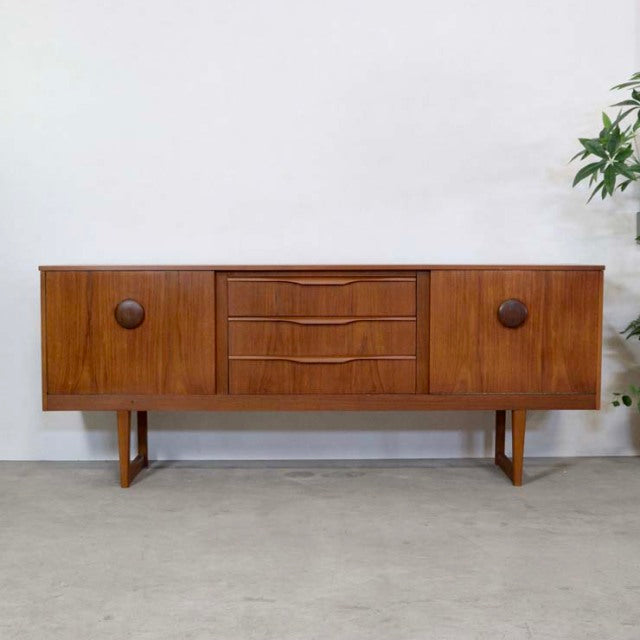 Vintage British teak sideboard with mid-century design, distinct peg legs, and rounded wooden handles.