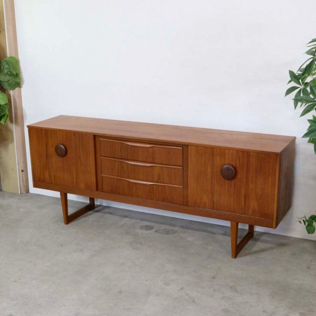 Mid-century British vintage teak sideboard featuring rounded wooden handles and tapered legs with visible wood grain from.