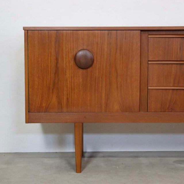 Mid-century British vintage teak sideboard with textured wood grain, round wooden handle, and slender tapered legs from.