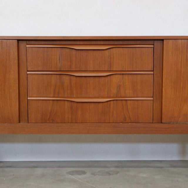 Mid-century British vintage teak sideboard with distinctive carved handles and rich wood grain on tapered legs from Denmark.