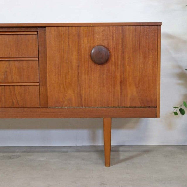 Mid-century British vintage teak sideboard with distinctive circular door handle, straight legs, and smooth wood grain.