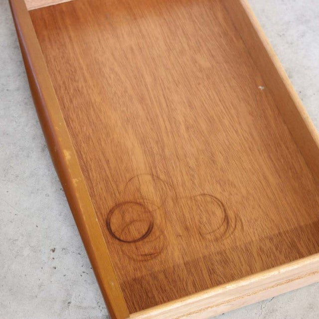 Close-up of vintage teak wood drawer with clear mid-century British grain and circular stains on smooth surface.