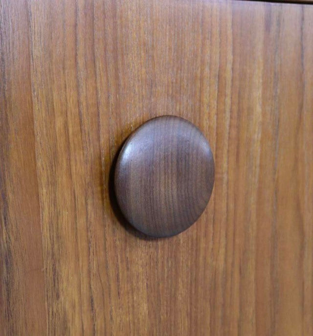 Close-up of vintage teak sideboard door with round, dark wood British mid-century handle, showcasing smooth grain texture.