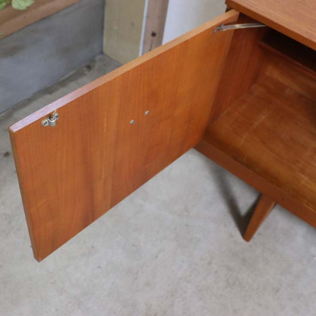 Mid-century British vintage teak sideboard door open, showcasing rich wood grain and unique angled legs from Denmark design.