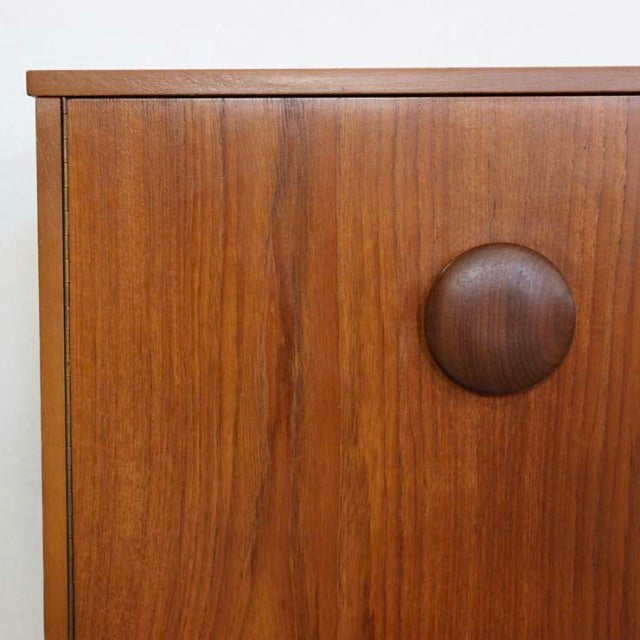 Close-up of vintage British mid-century teak sideboard door featuring prominent circular wooden handle and rich wood grain.