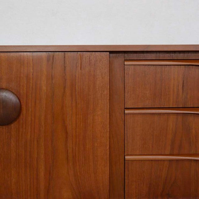 Mid-century British vintage teak sideboard with textured wood grain, distinctive rounded handle, and sleek drawers.